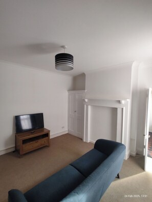A living room with a blue sofa, a wooden TV stand, a white fireplace, and a ceiling light fixture. - Stylish 2 Bedroom Apartment in Havant (Havant)