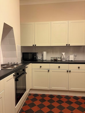 A kitchen with white cabinets, a black countertop, a microwave, a stove, and a checkered floor. - Stylish 2 Bedroom Apartment in Havant (Havant)
