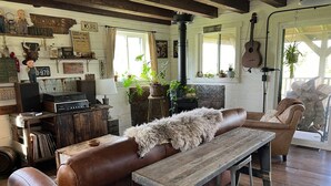 A rustic interior with a leather couch, wooden table, and various decorative items including plants and vintage objects. - Driftless Log Cabin w/ Kickapoo Valley View (Readstown)
