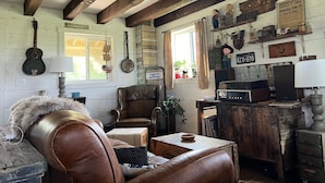 A rustic room with wooden beams, a leather sofa, a wooden cabinet, and various wall decorations including signs and a guitar. - Driftless Log Cabin w/ Kickapoo Valley View (Readstown)