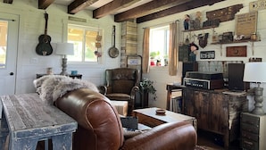 A rustic room with exposed wooden beams, a leather sofa, a wooden table, and various vintage decorations. - Driftless Log Cabin w/ Kickapoo Valley View (Readstown)