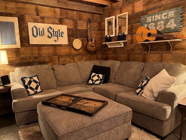 A cozy living room with a wooden wall, a sofa, a coffee table, and a guitar. - Driftless Log Cabin w/ Kickapoo Valley View (Readstown)