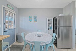 A compact kitchen with a round table, four chairs, a stainless steel refrigerator, and a small cabinet.