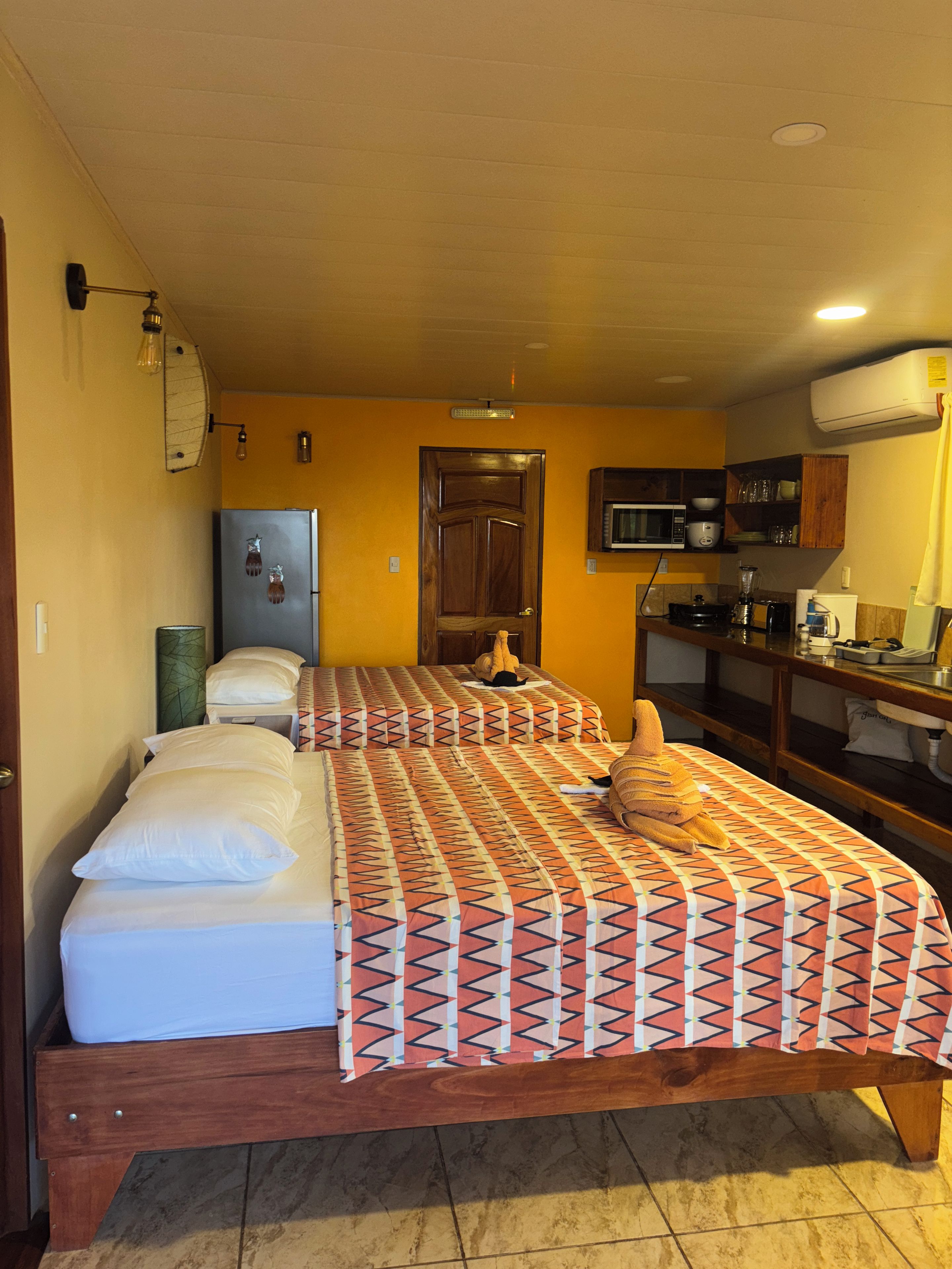 Une petite chambre avec deux lits, un coin cuisine et une porte.