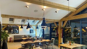 A restaurant with wooden beams, hanging pendant lights, and a large window with a city view. Tables are set with glasses and cutlery. - Squirrels Leap: Lake View with Spa Access (Somerford Keynes)
