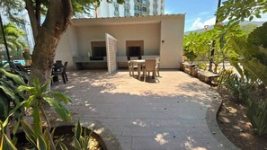 Un patio con mobiliario exterior, una zona de estar techada y vista a un edificio en el fondo.