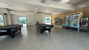 Une salle de billard avec deux tables, des distributeurs automatiques et une vue sur l’extérieur.