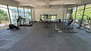 Ett gym med olika typer av träningsutrustning, stora fönster och ett klinkergolv.