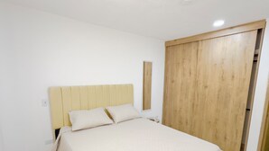 A bedroom with a bed, a wooden wardrobe, and a nightstand. - Modern Apartment with a Spectacular Ocean View (Santa Marta)