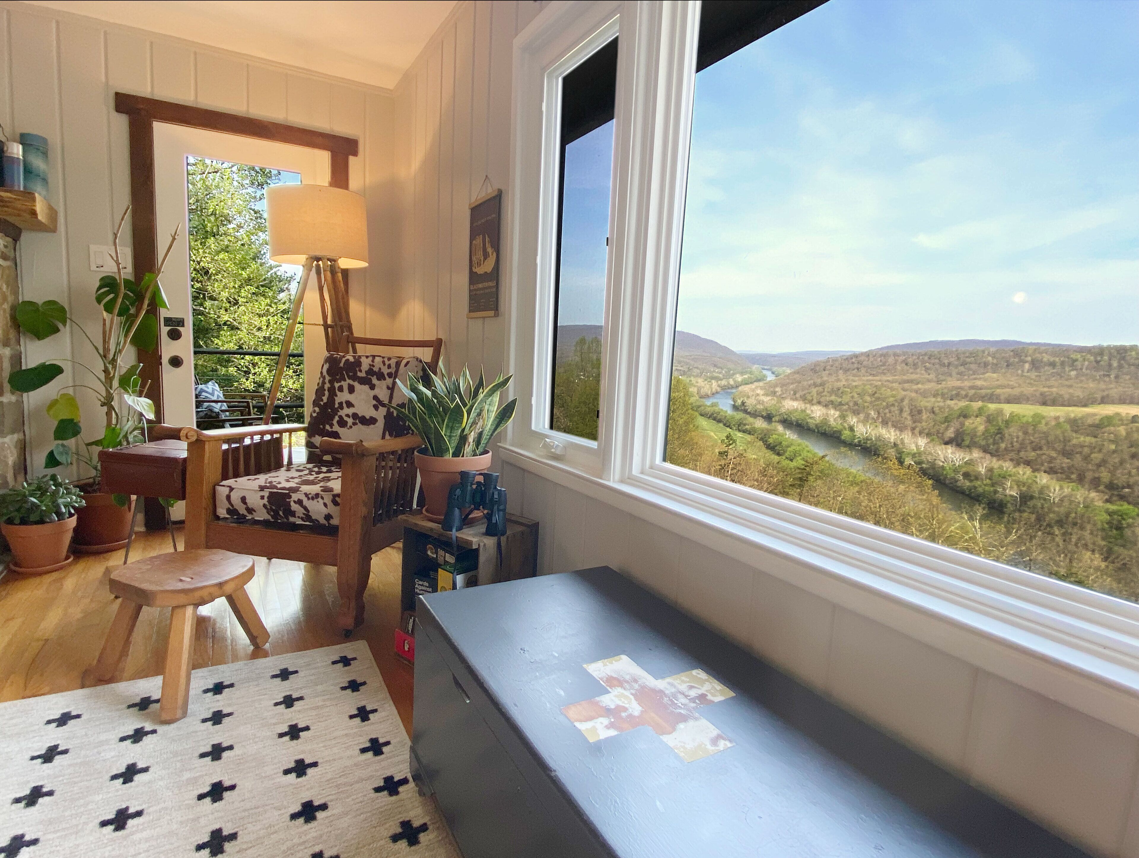 A cozy room with a large window, a wooden chair, a small stool, and a bench.