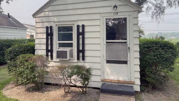 Una casa pequeña de un solo piso con techo a dos aguas, una puerta principal y un pequeño porche.