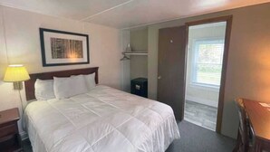 Una habitación de hotel con cama, lámpara de noche, un cuadro en la pared, armario y puerta que da a un balcón.