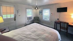 Habitación de hotel con una cama grande, un escritorio con silla, un televisor y dos ventanas con persianas.