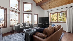 Un salon spacieux avec un plafond haut, de grandes fenêtres, un canapé en cuir, un téléviseur et une table basse.