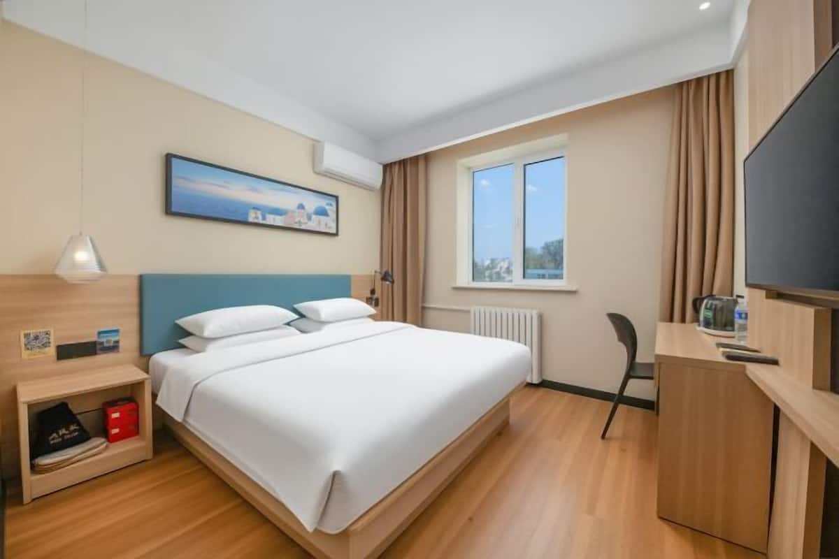 A hotel room with a bed, a desk, a chair, a window, and a painting on the wall.