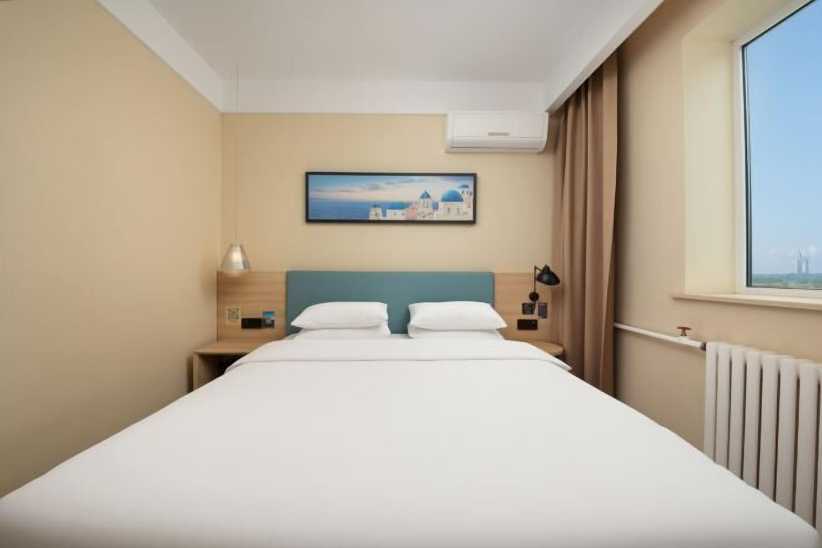 Ein Hotelzimmer mit Bett, Nachttisch, Lampe, einem Gemälde und einem Fenster mit Vorhängen.