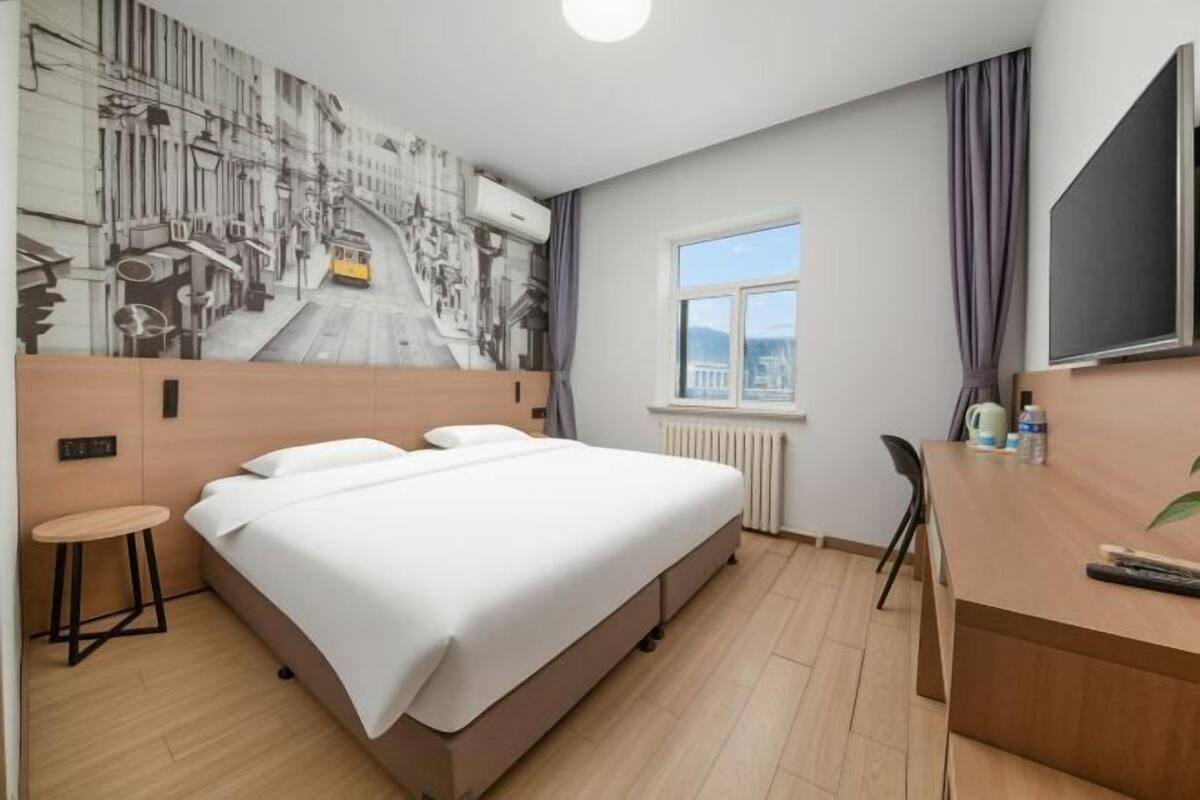 A hotel room with a bed, a desk, a chair, a window with a view, and a wall mural.