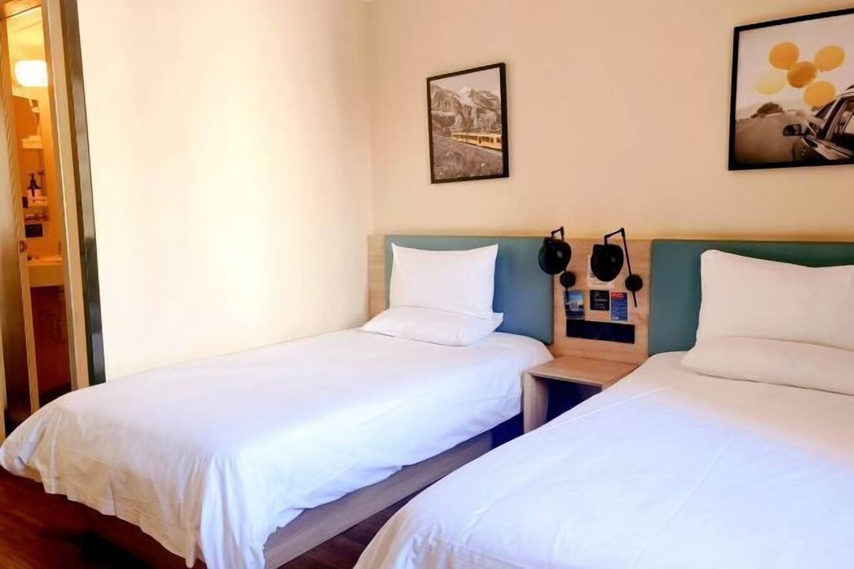 A hotel room with two single beds, a wooden headboard, a nightstand with a lamp, and a framed picture on the wall.
