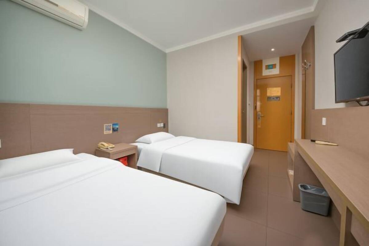 A hotel room with two beds, a desk, a TV, and a trash bin.