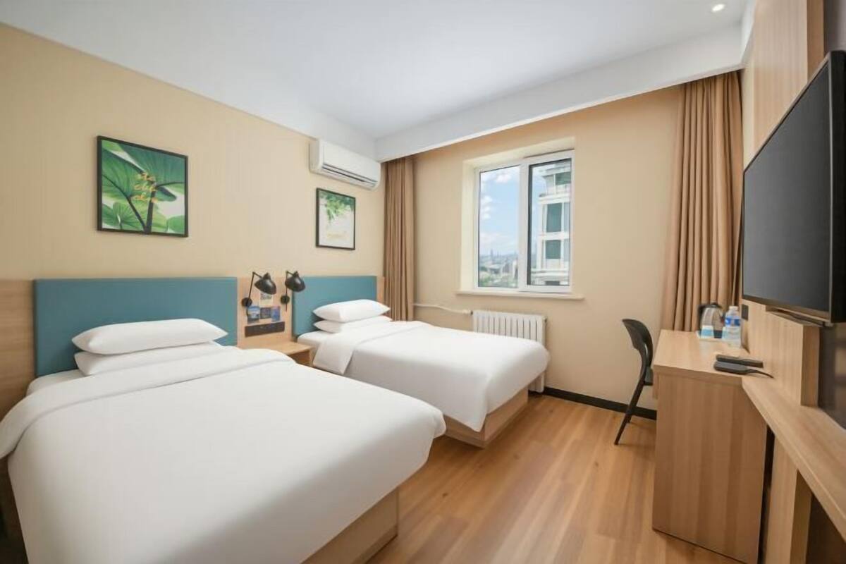 A hotel room with two beds, a desk, a chair, a TV, and a window with curtains.