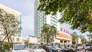 Un estacionamiento con varios coches, un edificio con señalización y un árbol en primer plano.
