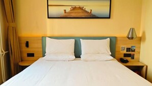 Habitación de hotel con cama, dos almohadas, cabecera de madera, mesita de noche con lámpara y un cuadro de un muelle en la pared.