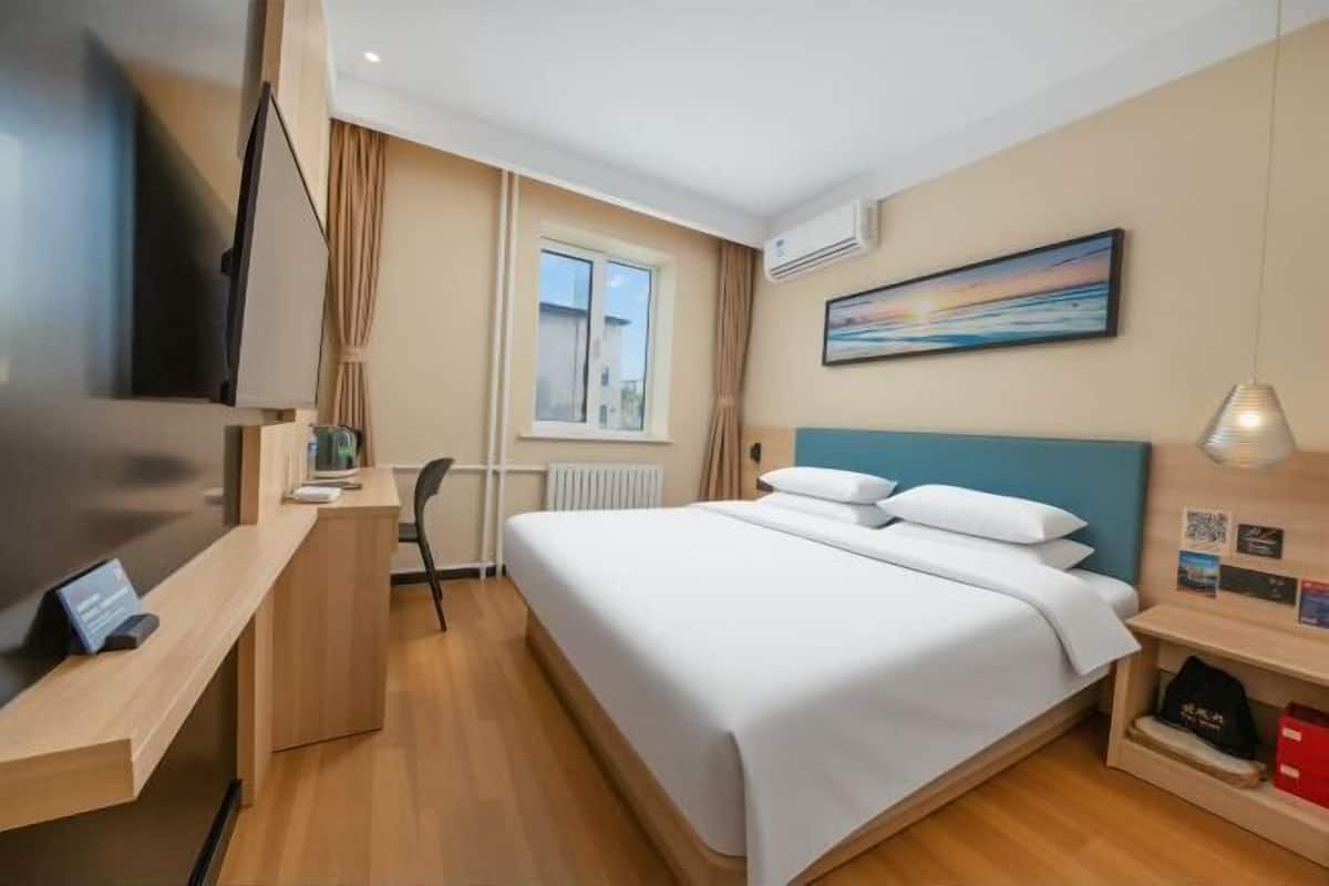 A hotel room with a bed, a desk, a chair, a TV, a window, and a painting on the wall.
