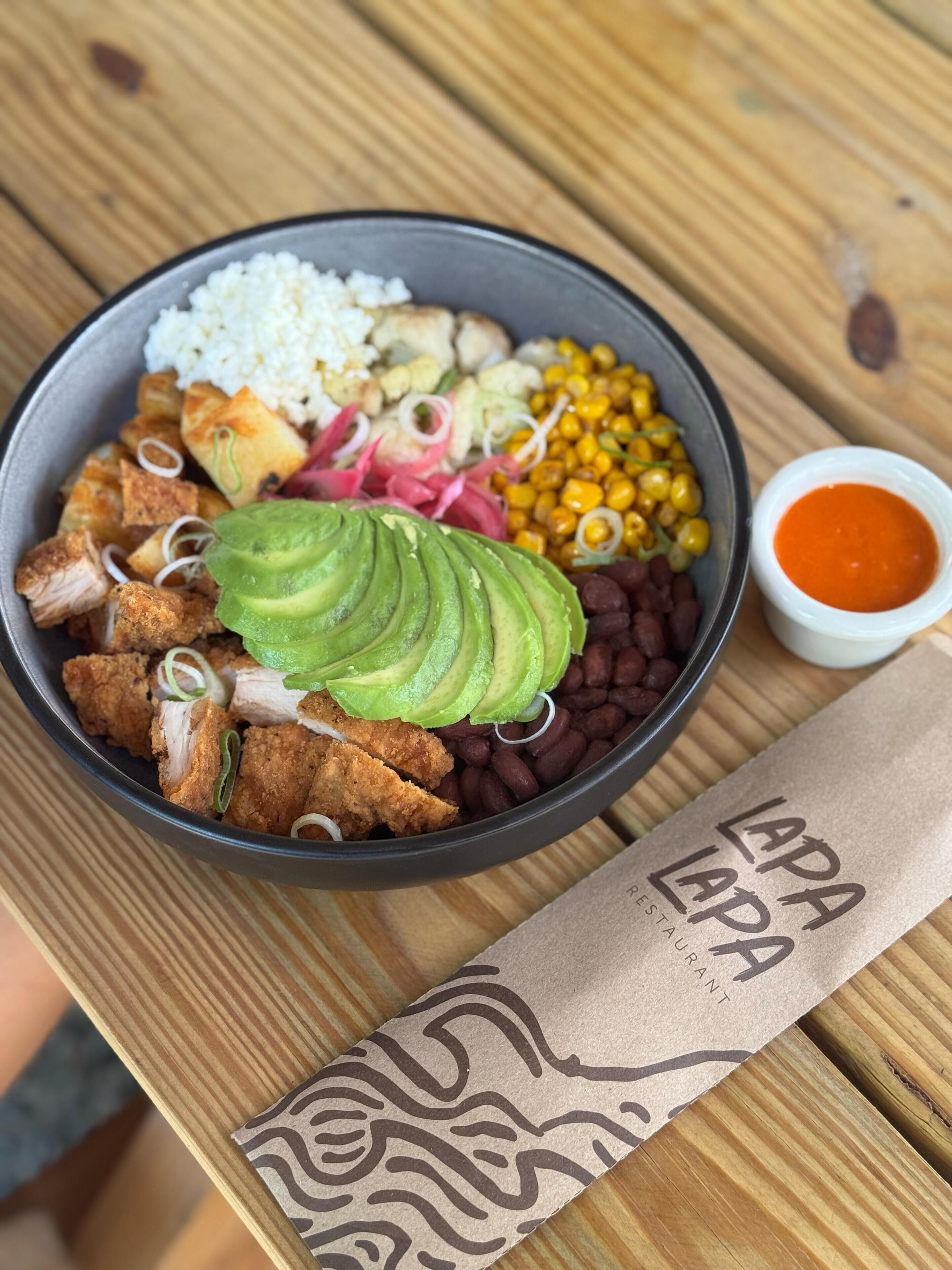 Eine Schüssel mit Essen, darunter Avocado, Bohnen und Mais, sowie eine kleine Saucenportion.