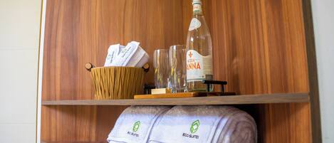 Una estantería de madera con una botella de agua, vasos, una cesta y toallas.