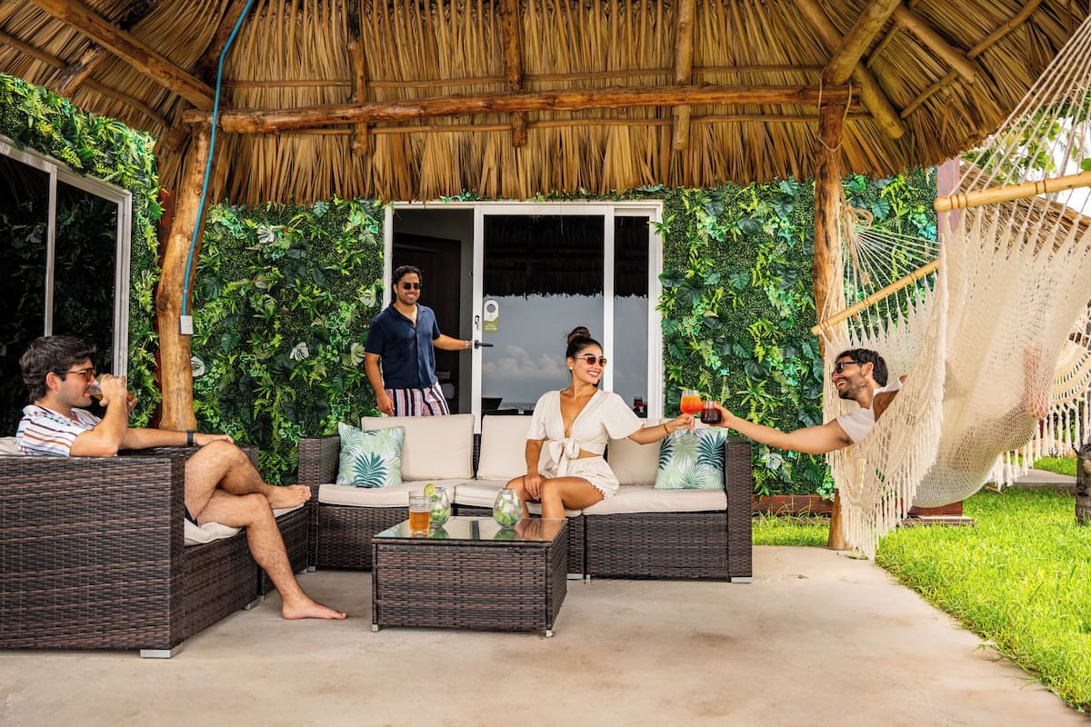 Un espacio al aire libre con techo, amueblado con ratán, una hamaca y un vidrio que da a una habitación.
