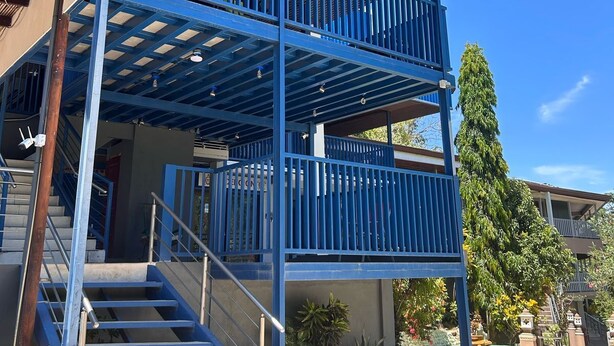 Un bâtiment à deux étages, à la façade bleue, doté d’un balcon couvert et d’un escalier menant à l’entrée.