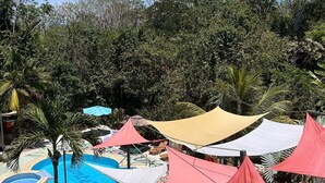 Un espace piscine agrémenté de plusieurs éléments aquatiques, entouré d’arbres et ombragé par des auvents aux couleurs vives.