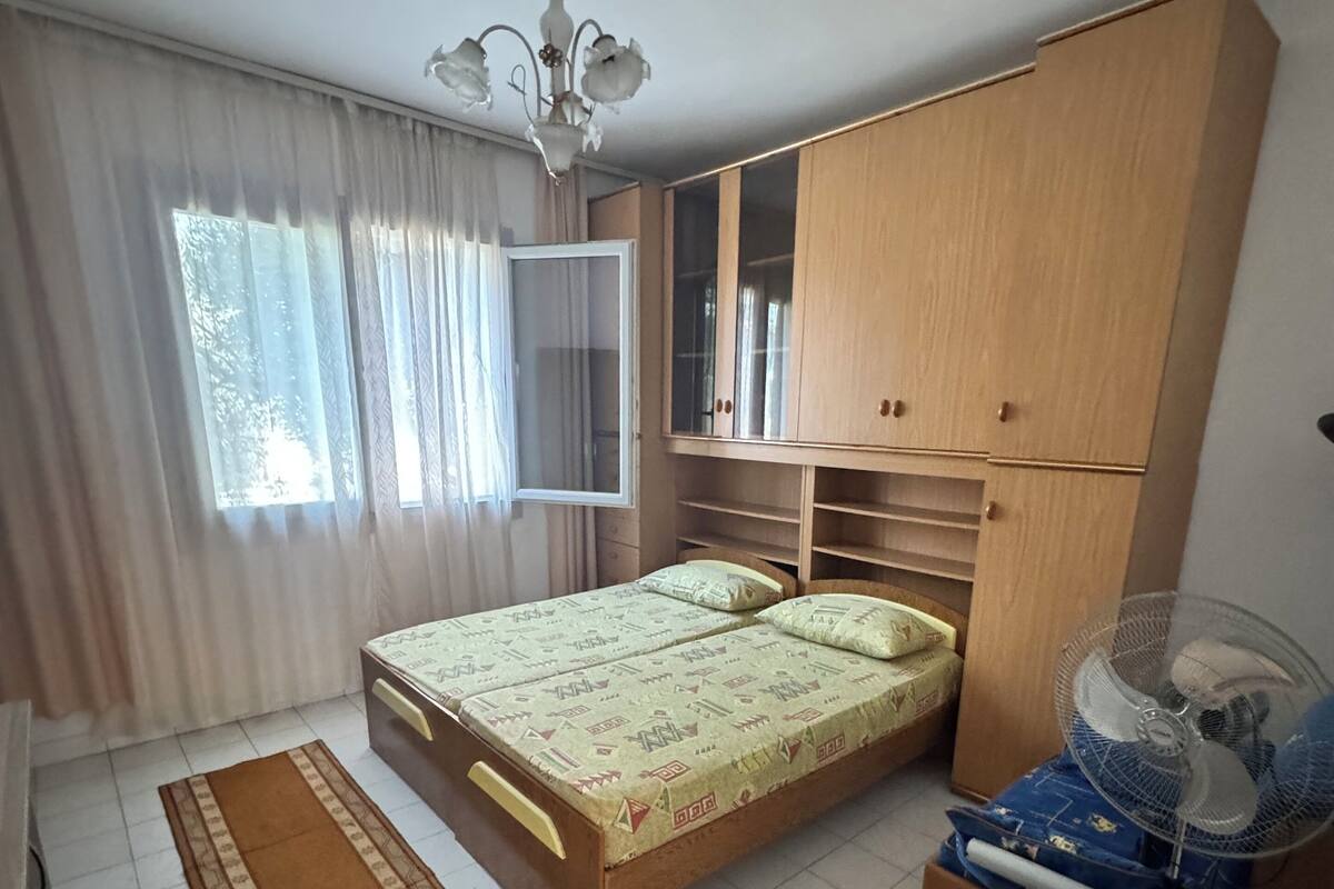 Une chambre à coucher avec un lit, une armoire, un ventilateur et une fenêtre avec des rideaux.