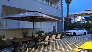 An outdoor seating area with tables and chairs, a parked car, and a palm tree. - VILA CANO (Durrës)