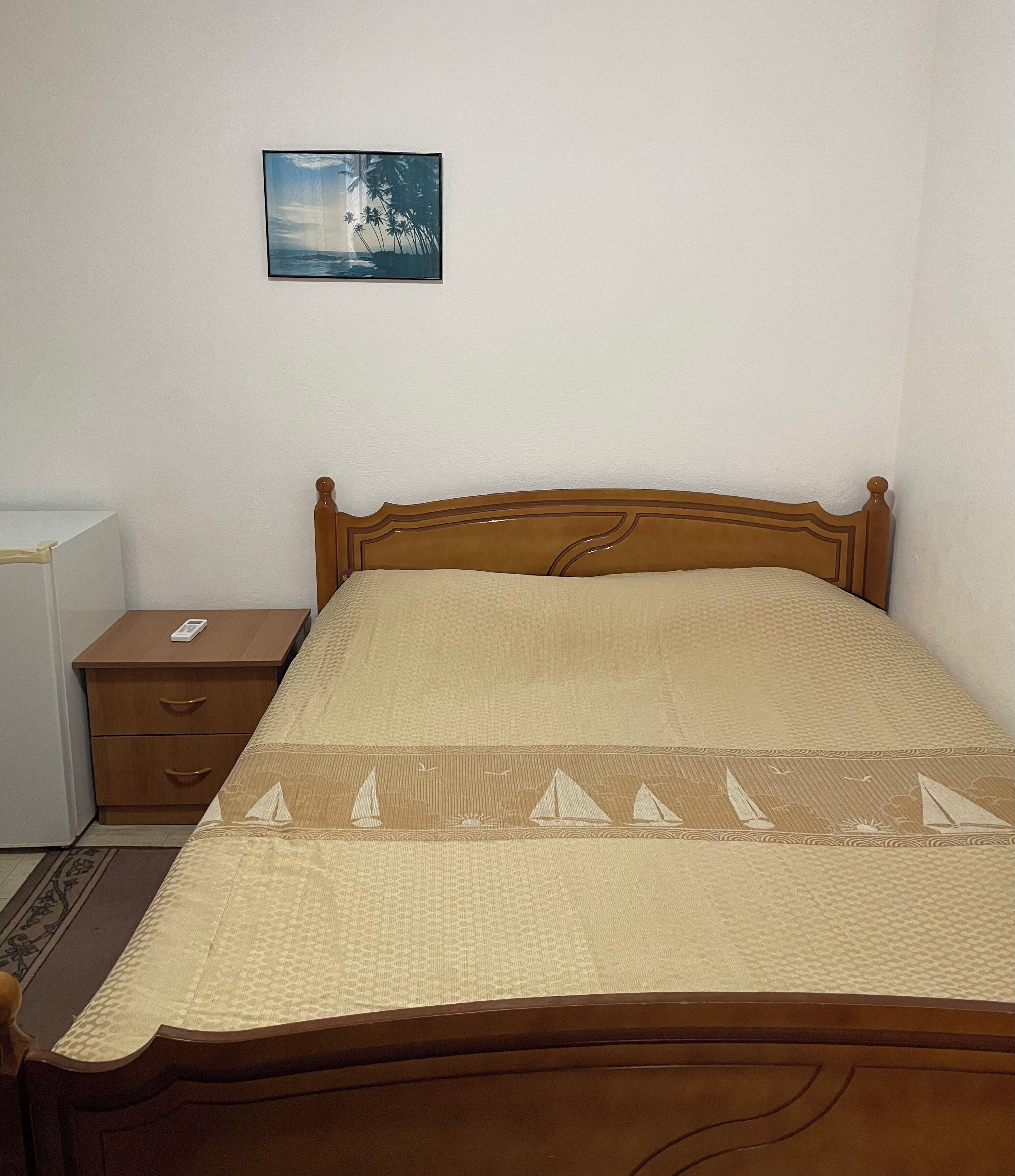 A neatly made bed with a patterned bedspread, a wooden headboard, and a bedside table with a remote control.
