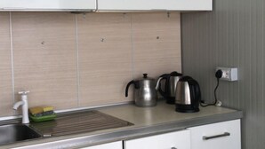 A compact kitchen with white cabinets, a stainless steel sink, and a kettle on the countertop. - VILA CANO (Durrës)