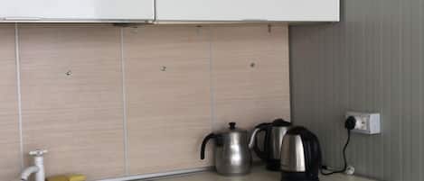 A compact kitchen with white cabinets, a stainless steel sink, and a kettle on the countertop.