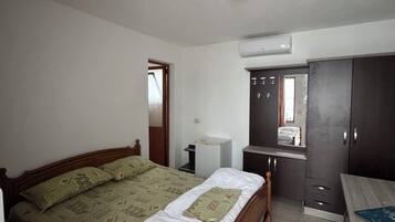 A bedroom with a wooden bed, a small desk, a wardrobe, and an air conditioning unit.