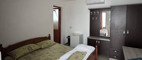 A bedroom with a wooden bed, a small desk, a wardrobe, and an air conditioning unit.