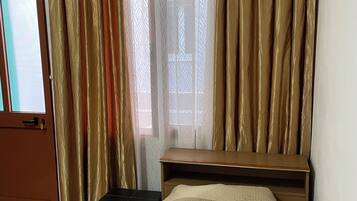 Una habitación con una cama, un escritorio, una silla, una puerta y una ventana con cortinas.