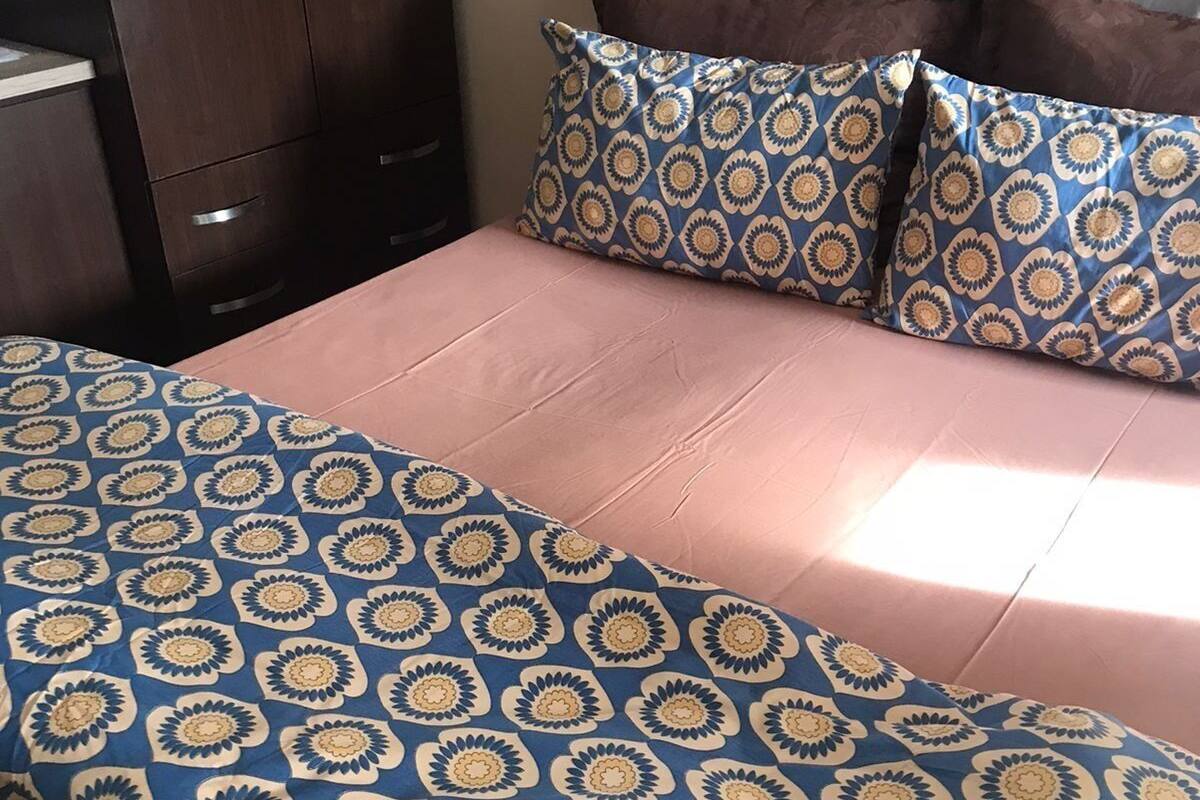 Un lit recouvert d’une couverture à motifs bleus et beiges, doté d’une tête de lit rembourrée grise et de deux oreillers marron.