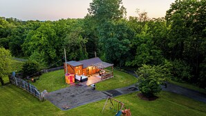 A wooden cabin with a patio, surrounded by a fenced yard and a swing set.