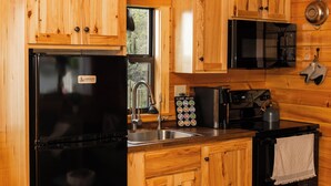 A compact kitchen with wooden cabinetry, a black refrigerator, a microwave, and a coffee maker. - Charming 2-bedroom tiny cabin hot tub camp fire sauna (Christiana)