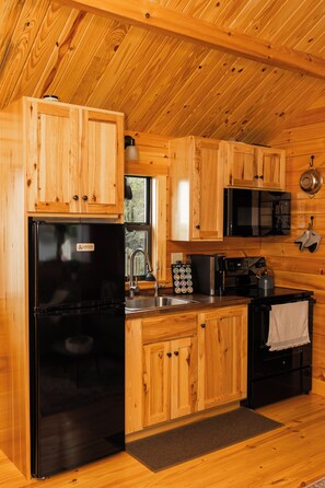 A compact kitchen with wooden cabinetry, a black refrigerator, a microwave, and a coffee maker.