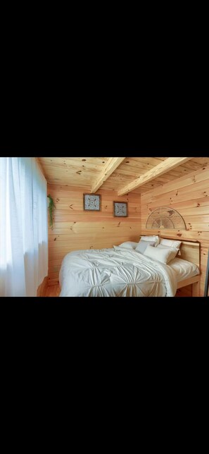 A wooden-paneled bedroom with a bed, two decorative wall pieces, and a ceiling fan.
