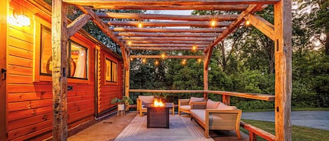 Une pergola en bois agrémentée de guirlandes lumineuses, un foyer extérieur et des sièges pour profiter de l’extérieur.