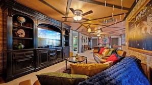 A spacious living room with a large flat-screen TV, leather sofas, and a ceiling fan. - 9-bedrooms ~ 25 Mins To Parks ~ Pool, Water Slides Hot Tub, Sauna, Mini Golf! (Davenport)