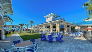 An outdoor patio with blue chairs and a round table, a covered seating area with umbrellas, and a view of the building in the background. - 9-bedrooms ~ 25 Mins To Parks ~ Pool, Water Slides Hot Tub, Sauna, Mini Golf! (Davenport)