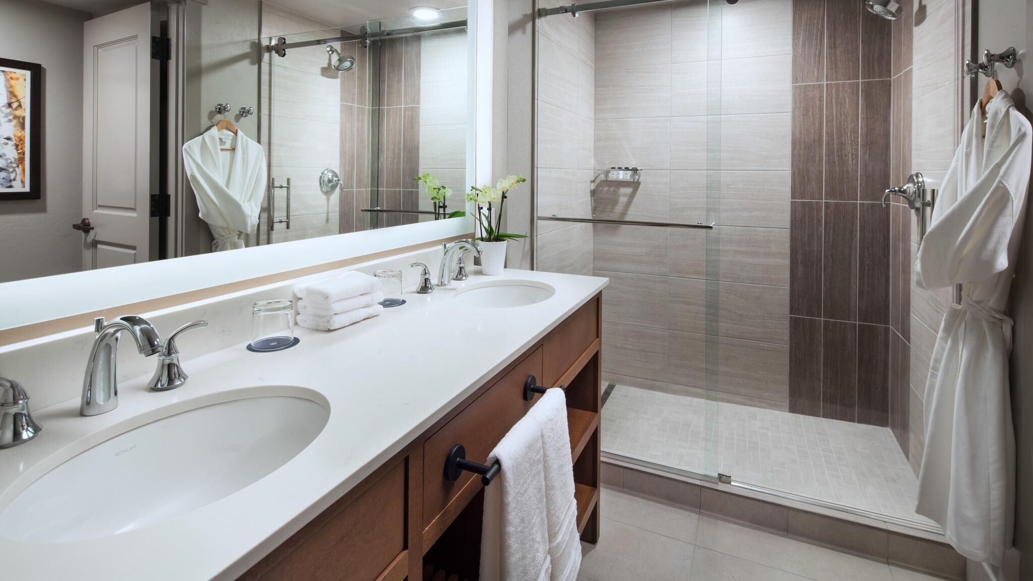 A modern bathroom with two sinks, a large mirror, and a walk-in shower.