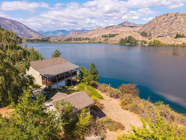 A house with a large deck overlooking a lake, surrounded by trees and hills.